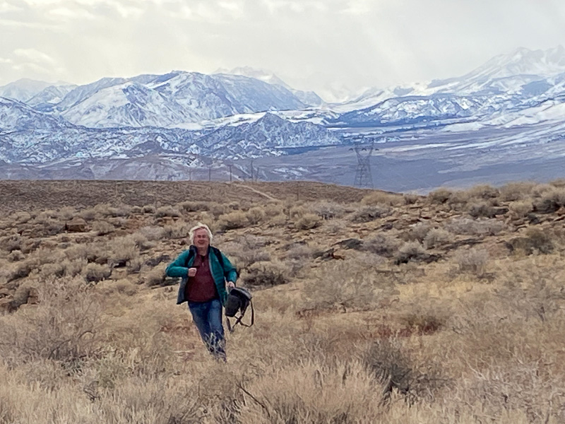 Roy running over Bishop Tuff with snowcapped moutains in background