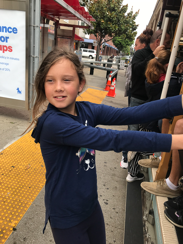 kate hanging on side of cable car in san francisco